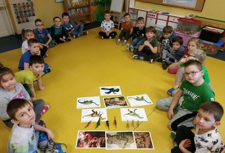 dzieci siedzą w kole z figurkami dinozaurów