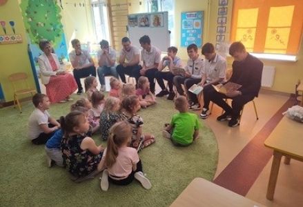 grupa dzieci przedszkolnych podczas głośnego czytania przez zaproszonych gości