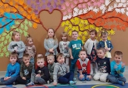 zdjęcie grupowe na tle kolorowego drzewa z wyciętych przez dzieci papierowych dłoni