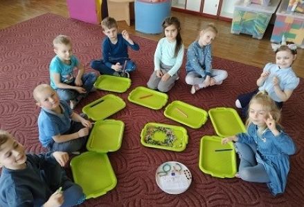 dzieci siedzą na dywanie przed tacami z kolorowymi koralikami