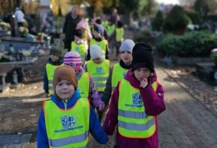 grupa dzieci przedszkolnych podczas spaceru na cmentarz i zapalania znicza przed Świętem Zmarłych