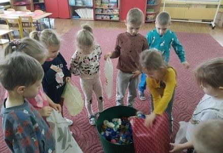 dzieci wrzucają nakrętki do pojemnika