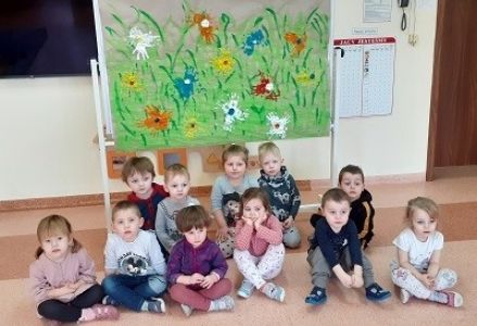 zjęcie grupowe, dzieci siedzą przed tablicą z namalowaną łąką