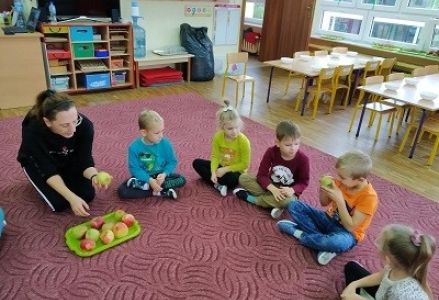 dzieci siedzą w kole wokoło jabłke