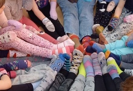 dzieci z wychowawcą siedzą w kole na dłoniach mają kolorowe skarpety