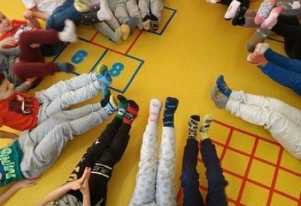 dzieci z wychowawcą siedzą w kole z nogami uniesiony do góry