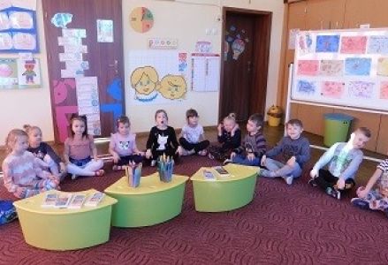 Dzieci siedza przed stoliczkami, a na nich znajdują się kredki
