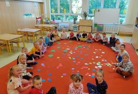 dzieci siedzą na dywanie z kolorowymi kopkami