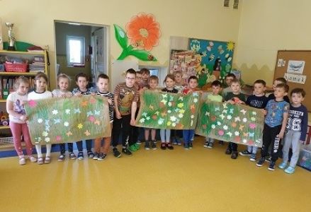 Dzieci stoją w jednej grupie i prezentują swoje prace