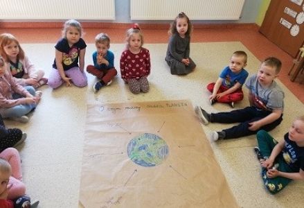 Dzieci siedzą przed plakatem z okazji dnia ziemii