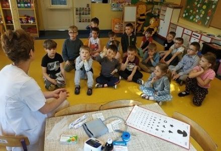 dzieci siedzą w grupie i patrzą na pielęgniarkę