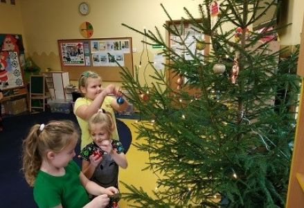 dzieci w sali przedszkolnej ubierają choinkę